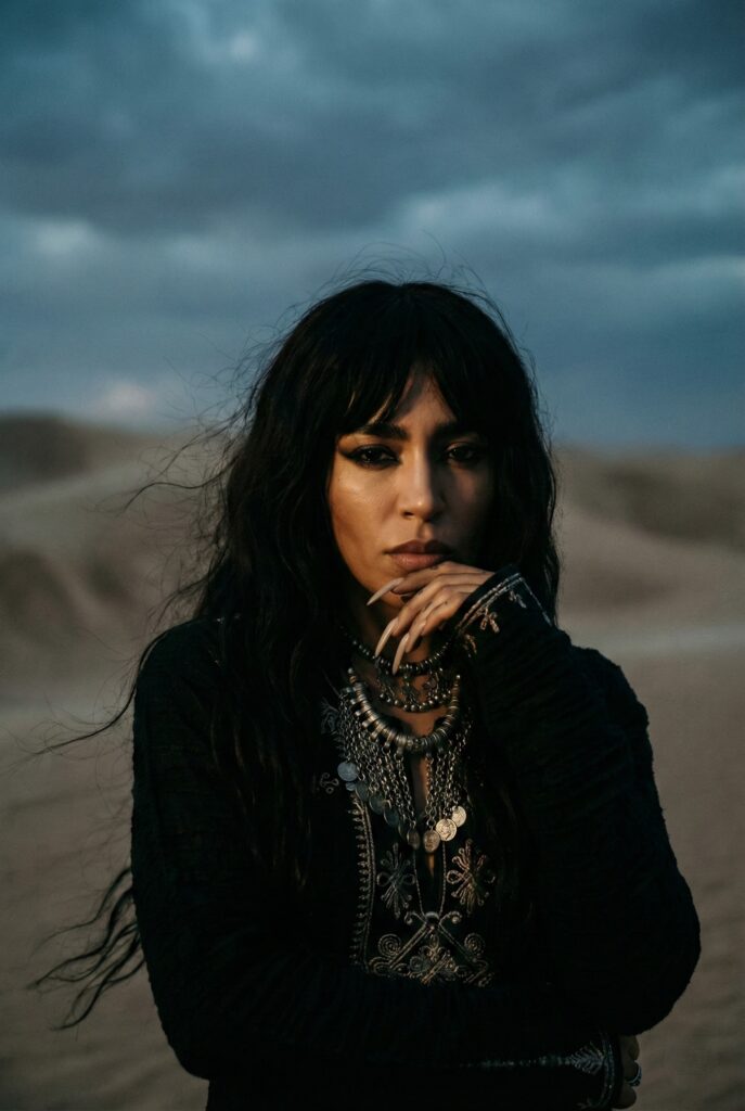 Portrait artistique de la chanteuse suédoise Loreen, double gagnante de l'Eurovision. Elle regarde intensément l'objectif, arborant de longs ongles et une coiffure sombre, dans une atmosphère mystique mélangeant influences nordiques et berbères.