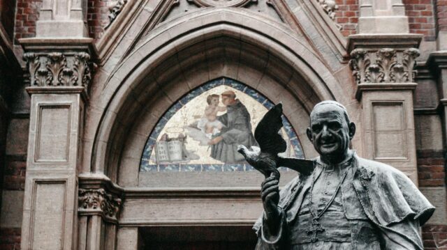 Pope Francis giving a speech in front of an Algerian flag