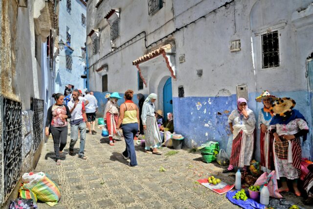 Woman wearing blue Chefchaouen attire walking in a bustling market street