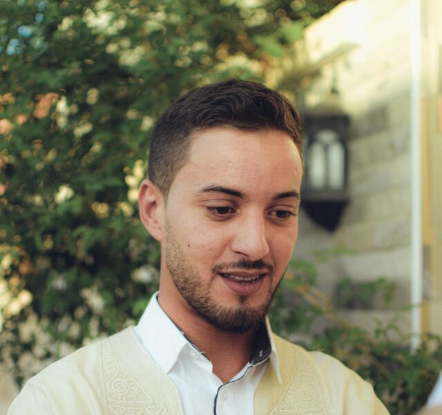 Jeune homme tunisien à Perpignan, étudiant de diplôme en main devant une porte rouillée