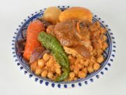 Recette traditionnelle tunisienne : Couscous au poulet et safran Tunisian chicken saffron couscous on a colorful tablecloth with steaming bowls and lemon wedges