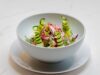 Recette Marocaine Rapide : Salade du Printemps, Une Délicieuse Décision en Version Apéro Salade du Printemps Marocaine avec avocat, tomates et olives sur une assiette de verre à côté d'un plafond marocain