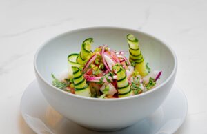 Recette Marocaine Rapide : Salade du Printemps, Une Délicieuse Décision en Version Apéro Salade du Printemps Marocaine avec avocat, tomates et olives sur une assiette de verre à côté d'un plafond marocain