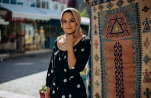 La mode contemporaine pour femme maghrébine : entre tradition et style moderne Femme maghrébine portant un hijab moderne et une robe traditionnelle au milieu d'un marché de textiles