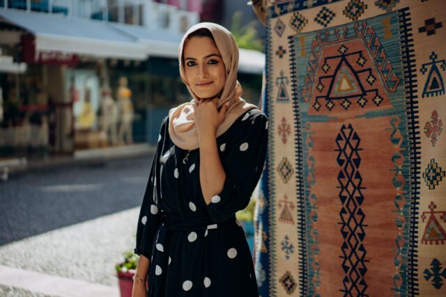 Femme maghrébine portant un hijab moderne et une robe traditionnelle au milieu d'un marché de textiles