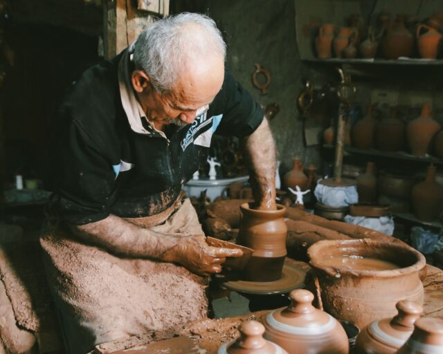 Tunisian potter working at his wheel with finished pottery on table