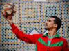 Achraf Hakimi : l’icône mode des Lions de l’Atlas Achraf Hakimi en costume de footballeur marocain posant devant un fond rouge
