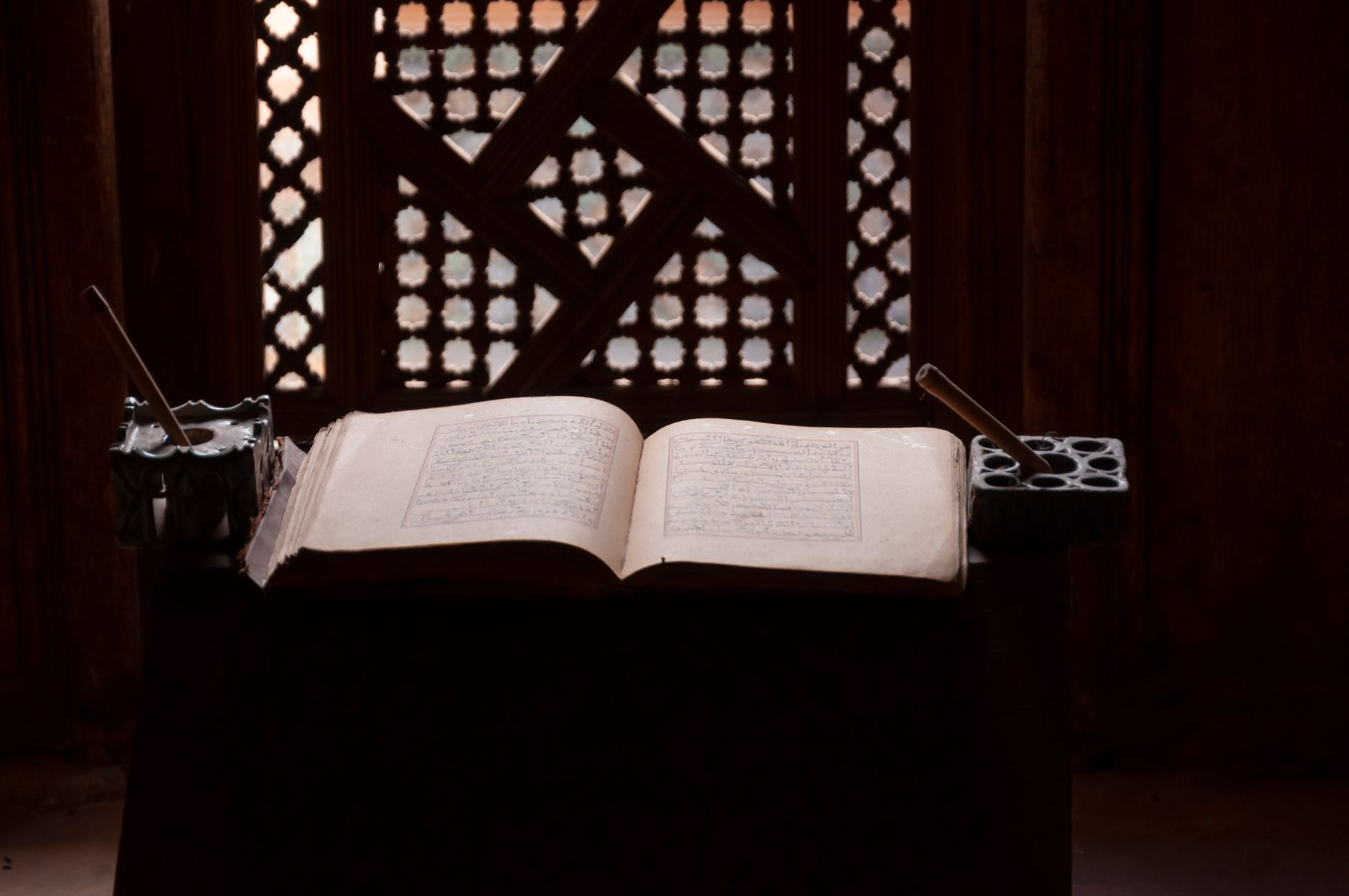 Rachid Ismaili écrivant un livre sur une table avec des livres de culture marocaine derrière lui